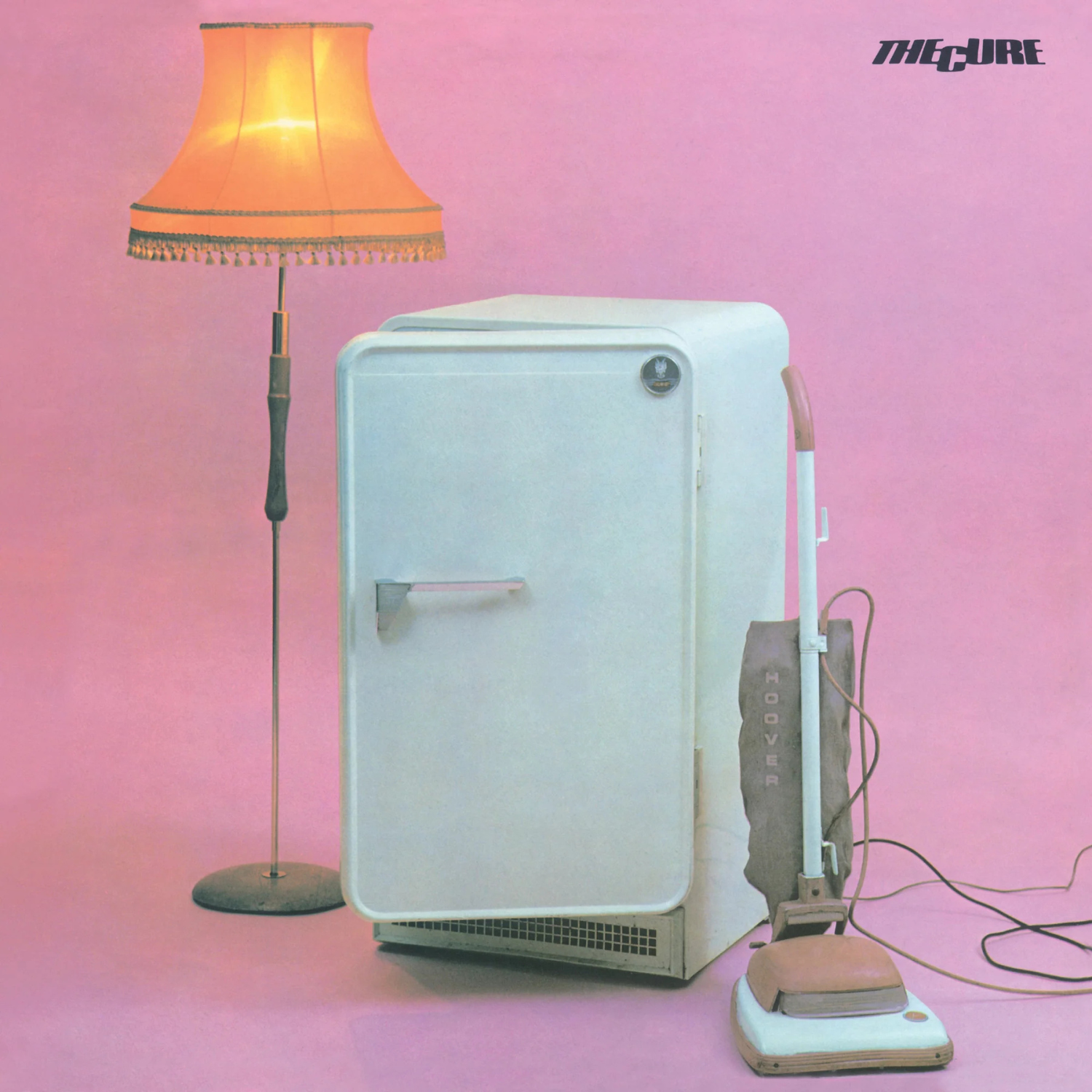 Album cover with a refrigerator, lamp, and vacuum cleaner on a pink background, featuring the band The Cure.